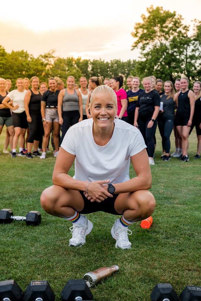 En coach sitter lågt nära marken och ler, med ett kvinnligt communityteam stående bakom henne.